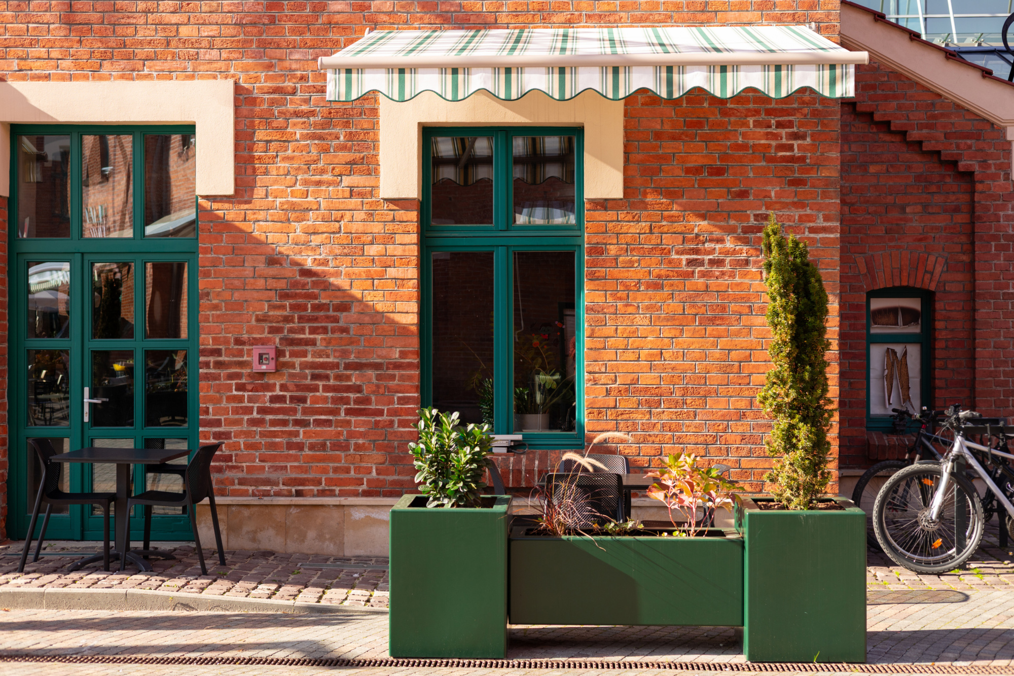 Street cafe with brick walls and canopy exterior design. Front view, sunny day. An outdoor cafe with tables, chairs. Lush green plants growing in pots near house.